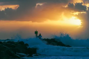 Surfer Contemplates Entering the Water as the Surf Pounds North Jetty
