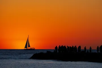 Venice Jetty: Onlookers Watch a Sailboat Sail the Setting Sun