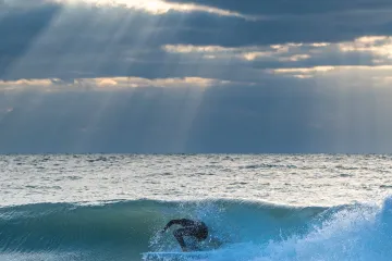 Harsh Light Through Clouds as Surfer Goes Under the Wave